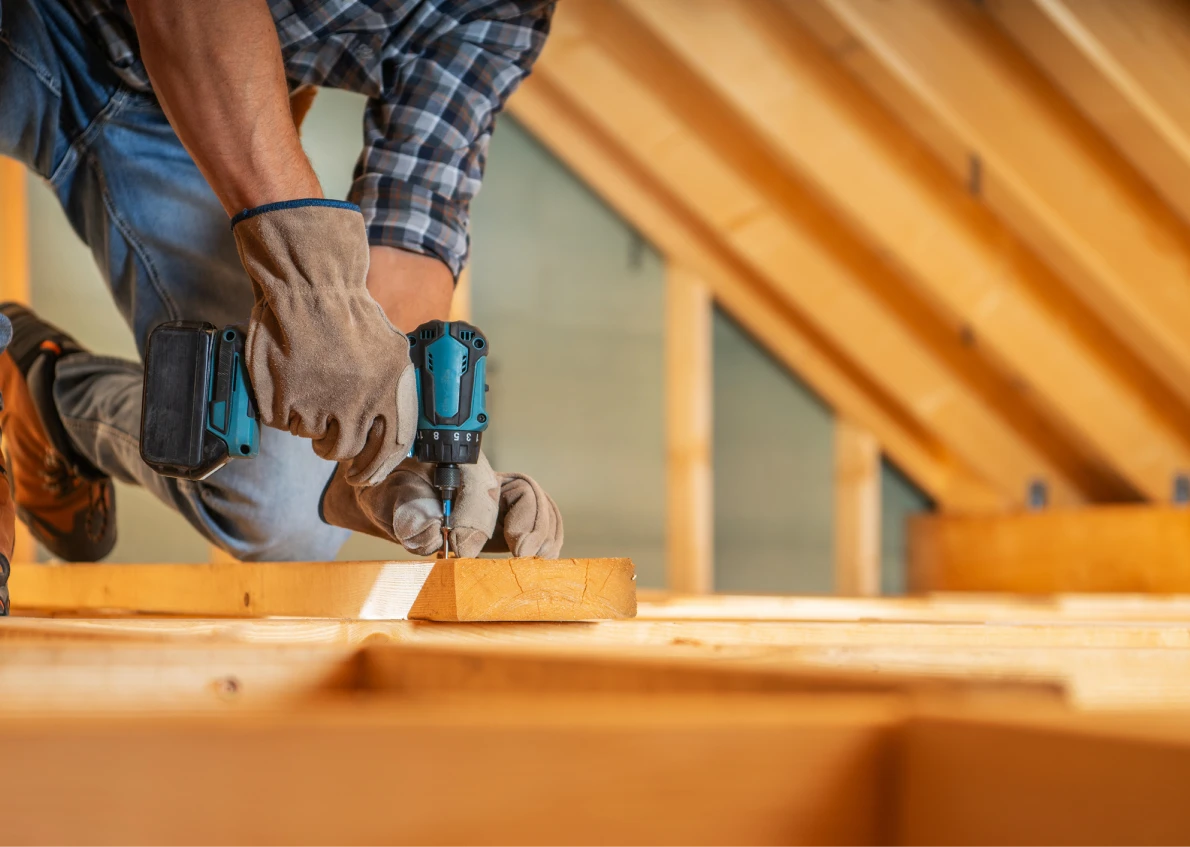 Worker using drill in attic construction.